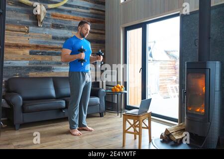 Ein Mann trainiert zu Hause mit Hanteln. Er verwendet ein Tutorial aus dem Internet. Übung für Bizeps. Gesundes Lifestyle-Konzept. Stockfoto