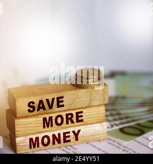 Sparen Sie mehr Geld auf Holzwürfel und 100 Euro Scheine und Münzen. Investitions- und Sparkonzept. Selektiver Fokus. Stockfoto