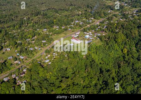 Ein langes rot-weißes Gebäude steht neben einer Straße mitten in einem Dorf an der Küste von Bougainville, Papua-Neuguinea, umgeben von Häusern unter Palmen. Stockfoto