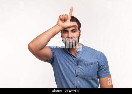 Unglücklich depressiver Mann mit Bart in blauem Hemd halten Hand in der Nähe der Stirn zeigt Verlierer Geste mit den Fingern, mit finanziellen und geschäftlichen Problemen. Stockfoto