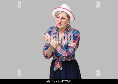 Schmerzen in der Hand oder am Handgelenk. Portrait von Kranken stilvolle reife Frau im lässigen Stil mit Hut und Brille stehen und hält Ihre schmerzhafte Handgelenk Hand. indo Stockfoto