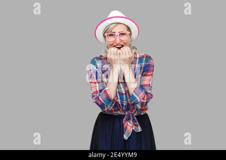 Portrait von traurigen nervös moderne, elegante, reife Frau im lässigen Stil mit Hut und Brille stehend, bitting Nägel und Suchen an Kamera und Panik. Stockfoto