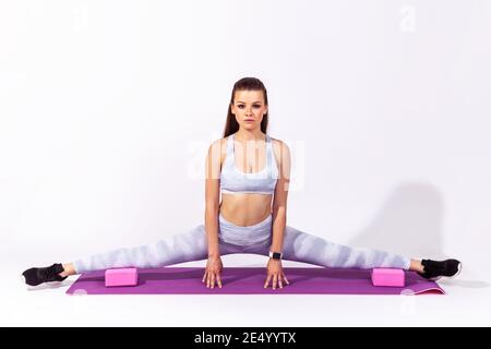 In voller Länge selbstbewusst sportliche Frau in weißem Top und Strumpfhosen Stretching ihre Beine dabei Splits auf Gummi Yoga Matte, Aufwärmen. Innenaufnahme im Studio Stockfoto