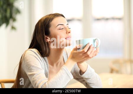 Glückliche Frau riecht Kaffee Aroma sitzen in einem Tisch an Zu Hause Stockfoto