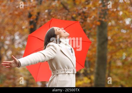 Glückliche Frau mittleren Alters atmen frische Luft im Winter mit Sonnenschirm in einem Park Stockfoto