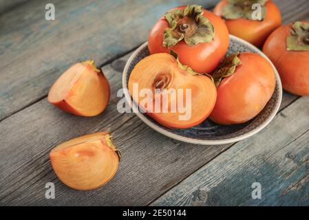 Frische Bio reife Persimmon Früchte in Schüssel mit Scheibe auf altem Holzhintergrund. Stockfoto