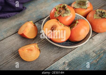 Frische Bio reife Persimmon Früchte in Schüssel mit Scheibe auf altem Holzhintergrund. Stockfoto