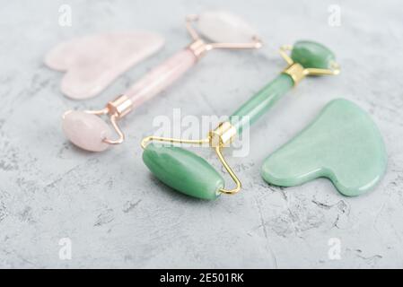 Gesichtsjade Massage Rollen und Gua Sha Massagegeräte aus gemacht Natürliche Jade und Rosenquarzstein auf grauem Hintergrund Stockfoto
