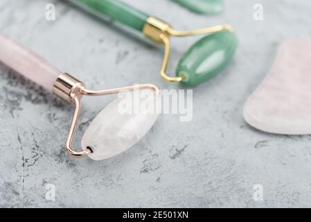 Gesichtsjade Massage Rollen und Gua Sha Massagegeräte aus gemacht Natürliche Jade und Rosenquarzstein auf grauem Hintergrund Stockfoto
