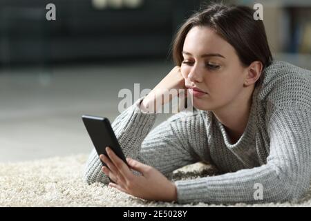 Gelangweilter Teenager, der Smartphone auf dem Boden liegend überprüft Zu Hause Stockfoto