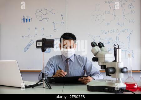 Naturlehrerin trägt Maske und Lehre online mit Smartphone in Das Klassenzimmer Stockfoto