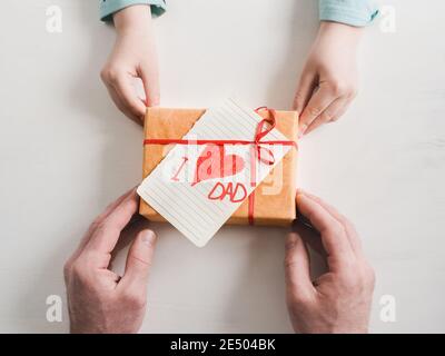 Die Hände des Kindes und die Hände des erwachsenen Mannes, schönen Geschenkkarton, Farbband und glasierte Plätzchen auf einem weißen, Holz- Hintergrund. Ansicht von oben, close-up. Vorbereitung für Th Stockfoto