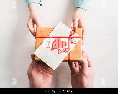 Die Hände des Kindes und die Hände des erwachsenen Mannes, schönen Geschenkkarton, Farbband und glasierte Plätzchen auf einem weißen, Holz- Hintergrund. Ansicht von oben, close-up. Vorbereitung für Th Stockfoto