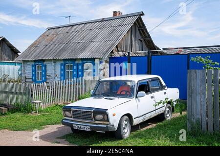 Traditionelles Holzhaus mit weißem Auto / Lada Riva / Lada Nova im ländlichen Dorf in Südsibirien, Russland Stockfoto