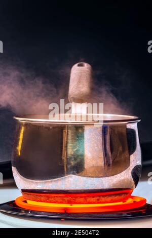 Vertikale Aufnahme eines dampfenden Topfes auf einem heißen Brenner auf einem weißen Herd. Stockfoto