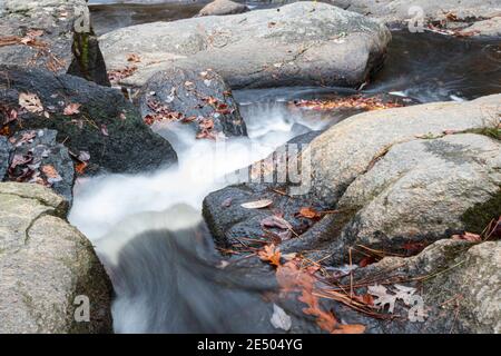Nahaufnahme des Wassers, das zwischen Felsen in einem Bach fließt, aufgenommen mit langer Belichtung. Stockfoto