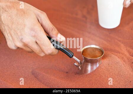 Kaffee, der auf der Straße auf traditionelle arabische Weise zubereitet wird, wird in roten heißen Sand gelegt, bis Flüssigkeit kocht Stockfoto