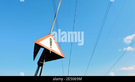 Rotes Dreieck mit Ausrufezeichen auf Stahlseil von elektrischem Pylon, klarer Himmel im Hintergrund Stockfoto