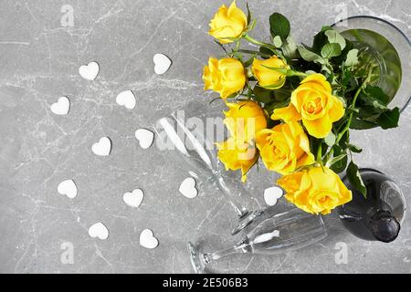 Gelbe Rosen, Flasche Sekt, Sektflöte und weiße Herzen auf grauem Hintergrund.Geschenk, Urlaub, Dating. Valentinstag, Muttertag, Frauentag Stockfoto