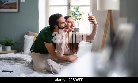 Junges Paar nimmt Selfie auf dem Bett drinnen zu Hause. Stockfoto