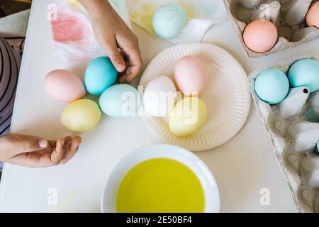 Nahaufnahme bunt gefärbte ostereier in Kinderhänden. Kind bereitet sich auf Ostern vor und färbt Eier mit flüssiger Lebensmittelfarbe. Blick von oben, Pastellfarben Stockfoto