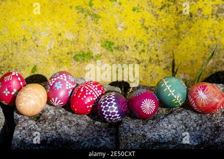 Sonnige gelbe Wand und Steine mit Ostereiern aus Deutschland handgefertigt mit Wachstechnik, alte ostdeutsche Tradition, Handwerkskunst, Maßanfertigung Ost Stockfoto