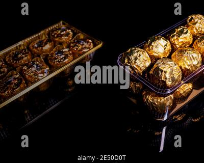 Eine Schachtel runder Pralinen in goldener Verpackung auf schwarzem Hintergrund. Runde Bonbons. Goldene Farbe. Ein Weihnachtsgeschenk. Geburtstag. Food-Foto. Süßes Essen. Ha Stockfoto