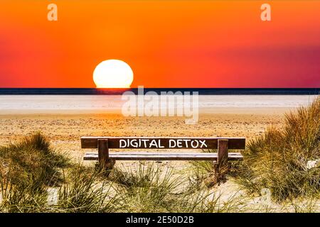 Die Worte Digital Detox geschrieben auf einer Bank mit Blick Des Sonnenuntergangs am Meer Stockfoto