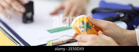 Patient hält ein Glas Marihuana in den Händen. Arzt legt Stempel auf Dokument Stockfoto