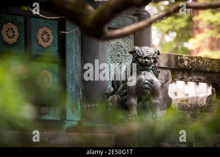 Nahaufnahme einer Bronzestatue eines japanischen Löwen Vor dem Tempel von Vegetation umgeben Stockfoto