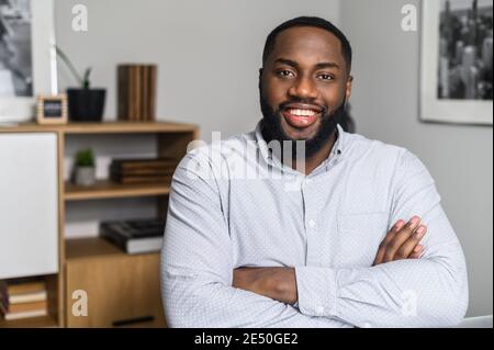 Glücklicher afroamerikanischer Firmenchef CEO, der mit gekreuzten Armen im Büro steht. Porträt eines erfolgreichen lächelnden Unternehmers, selbstbewusst Stockfoto
