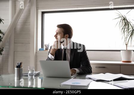 Nachdenklicher Geschäftsmann berührt Kinn, Blick zur Seite, erwägen Aufgabe Stockfoto