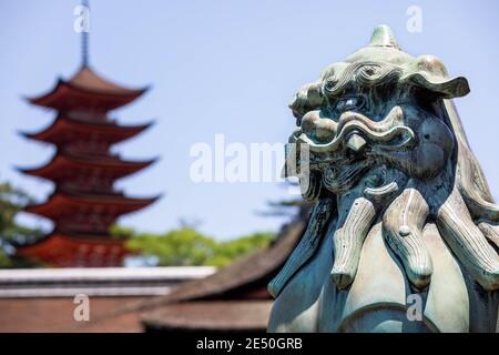 Nahaufnahme einer Bronzestatue eines japanischen Löwen, mit einer roten Pagode im Hintergrund Stockfoto