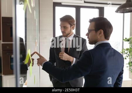 Selbstbewusster Geschäftsmann mit Brille, der mit Kollegen über Haftnotizen spricht Stockfoto