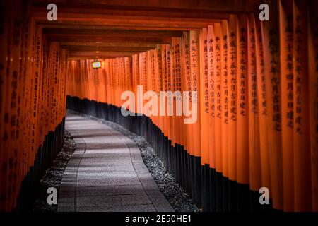 Der Innenraum eines Votivtunnels aus einer Reihe von Rote Holztorii mit schwarzen Kanji-Gebeten Stockfoto