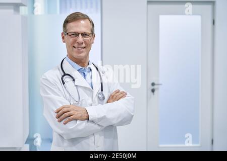 Lächelnder reifer Oberarzt, der im Krankenhaus steht und die Kamera anschaut. Stockfoto