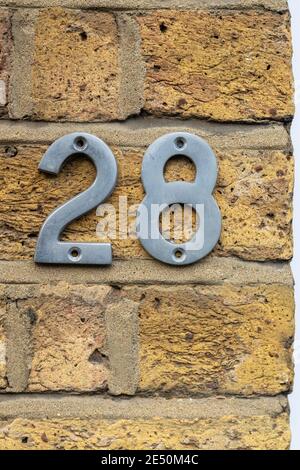 28 als glänzende Metallziffern auf einem rohen gelben Ziegel Wand Stockfoto