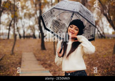 Eine sanfte junge Frau unter einem transparenten Regenschirm versteckt sich vor dem Wetter im Herbstpark. Hochwertige Fotos Stockfoto