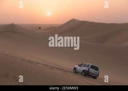 Ein Sportfahrzeug, das bei Sonnenuntergang Sanddünen auf einer Wüstensafari in der Wüste des leeren Viertels (Rub' al Khali) in der Nähe von Abu Dhabi, VAE, baschiert. Stockfoto