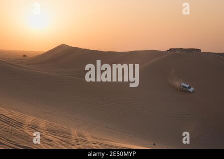 Ein Sportfahrzeug, das bei Sonnenuntergang Sanddünen auf einer Wüstensafari in der Wüste des leeren Viertels (Rub' al Khali) in der Nähe von Abu Dhabi, VAE, baschiert. Stockfoto