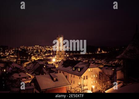 Nachtaufnahme von Fribourg (Schweiz) unter dem Schnee, mit der Kathedrale Saint-Nicolas in der Mitte Stockfoto