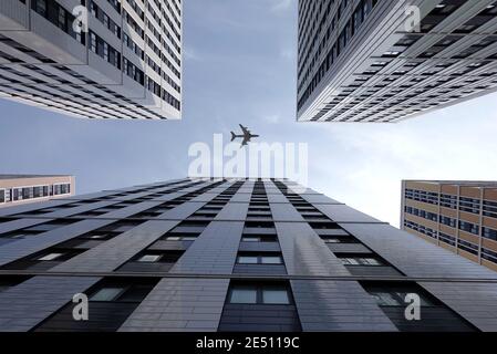Großes Flugzeug, das hoch über modernen Wolkenkratzergebäuden der Stadt fliegt Viele Fenster in Business-Cluster-Ansicht von unten nach oben auf hell Sonniger Tag Stockfoto