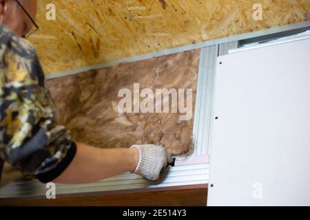 Isolierung des Hauses mit Mineralwolle. Ein Mann installiert einen Block aus wärmeisolierendem Material an der Wand für weitere Gipskartonverkleidungen. Stockfoto