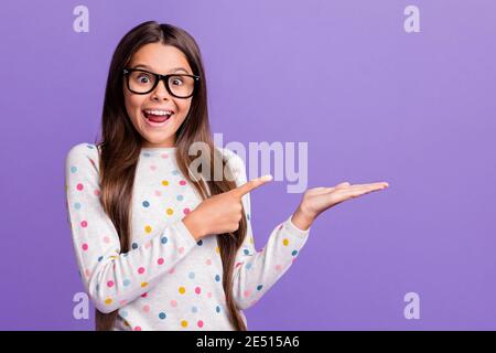 Foto-Porträt der kleinen Brünette in einer Brille zeigt auf blank Raum auf der Hand lachend isoliert auf hellviolettem Hintergrund Stockfoto