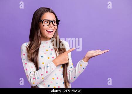 Foto-Porträt von Schulmädchen in Brille zeigt Blick auf Copyspace Auf der Handfläche lächelnd isoliert auf hellviolettem Hintergrund Stockfoto