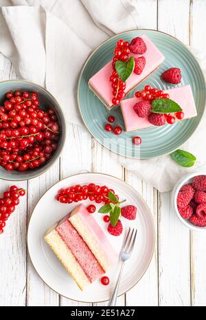 Köstliche und erfrischende saftige Dessert, Punch Cake mit Zuckerzuckerguss und frischen Himbeeren und roten Johannisbeeren auf Holz Hintergrund gekrönt Stockfoto