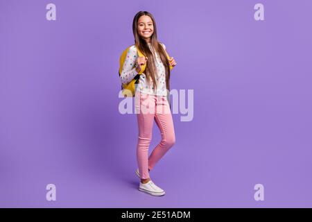 In voller Länge Körpergröße Foto von fröhlichen Schulmädchen mit langen Haare tragen gelben Rucksack isoliert auf lebendigen violetten Hintergrund Stockfoto