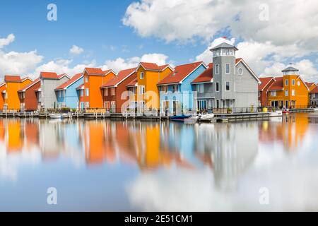 Symmetrische Nahaufnahme einer Gruppe von farbenfrohen modernen holländischen Häusern am Wasser, unter einem blauen Sommerhimmel mit geschwollenen Wolken Stockfoto