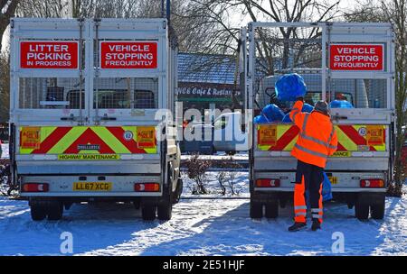 Zwei Lastwagen sammeln Müll im Schnee. Müllmann wirft Müllbeutel in die Rückseite des LKWs. Stockfoto