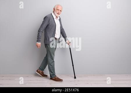 In voller Größe Profil Foto von optimistischen alten Mann gehen mit Zauberstab tragen dunkle Pullover Hose isoliert an der grauen Wand Stockfoto